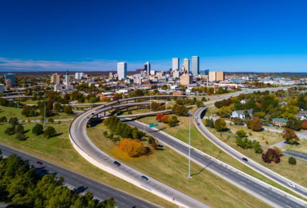 Aerial view of Downtown Tulsa skyline with grass, trees, and freeways in the foreground.
